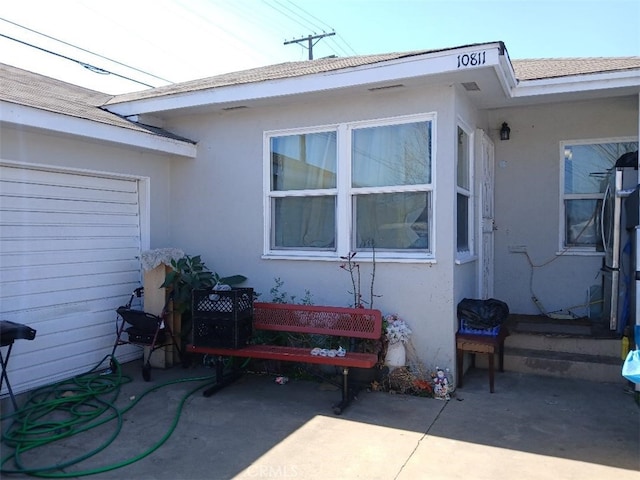 view of side of property with a shingled roof, a patio, and stucco siding