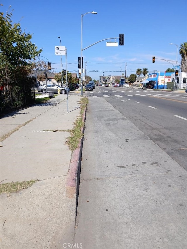 view of road featuring traffic lights, curbs, sidewalks, and street lights