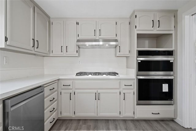 kitchen featuring light wood finished floors, light countertops, appliances with stainless steel finishes, white cabinetry, and under cabinet range hood