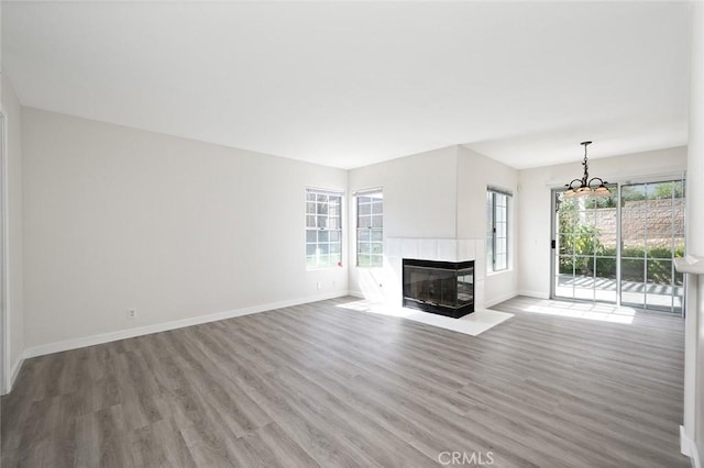 unfurnished living room featuring a tiled fireplace, wood finished floors, and baseboards