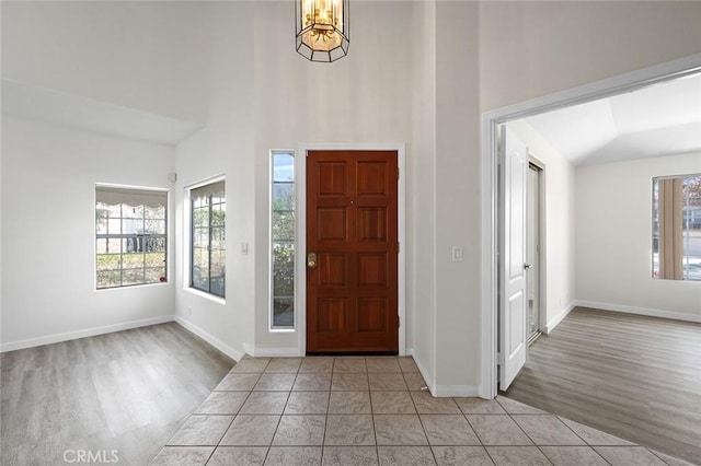 tiled foyer entrance with baseboards, high vaulted ceiling, and an inviting chandelier