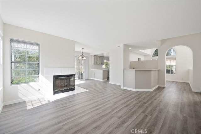 unfurnished living room featuring arched walkways, a tile fireplace, light wood-style flooring, and baseboards