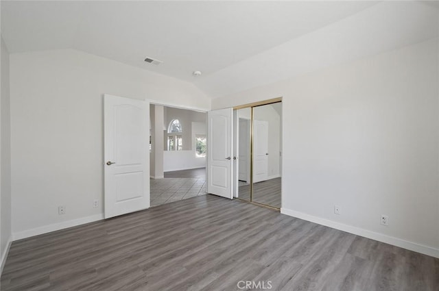 spare room with visible vents, vaulted ceiling, baseboards, and wood finished floors