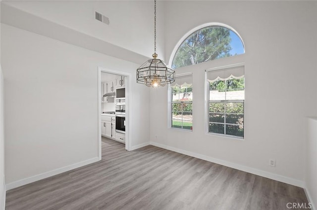 unfurnished dining area featuring a chandelier, wood finished floors, a towering ceiling, visible vents, and baseboards