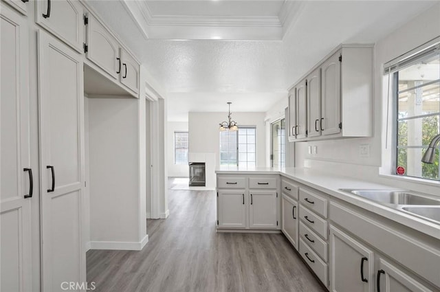 kitchen with a peninsula, a sink, light countertops, ornamental molding, and light wood-type flooring