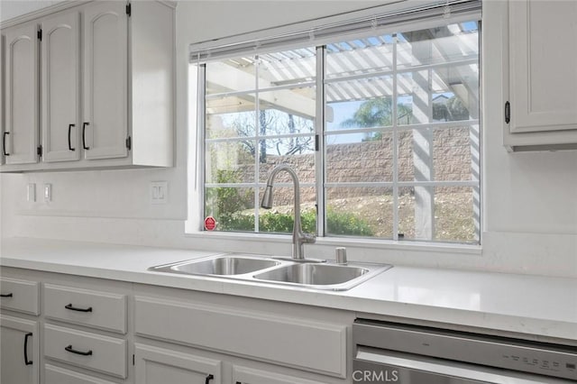 kitchen featuring stainless steel dishwasher, white cabinetry, light countertops, and a sink