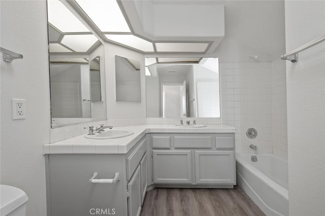 bathroom featuring washtub / shower combination, double vanity, a sink, and wood finished floors