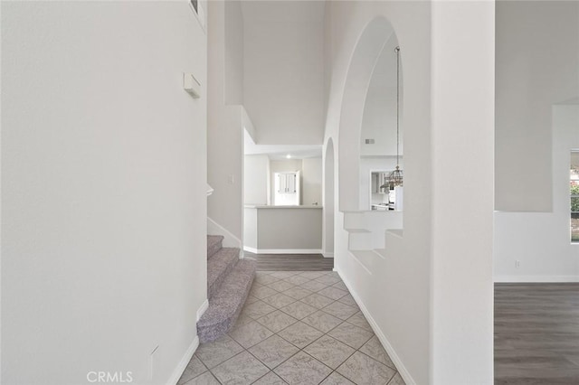 corridor featuring stairway, a high ceiling, and baseboards