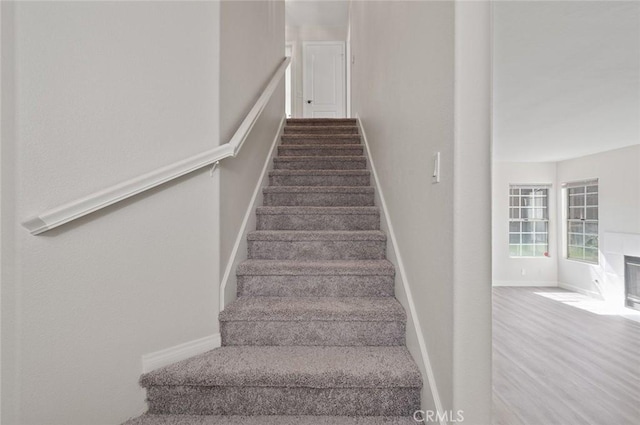 stairs with wood finished floors, a fireplace with flush hearth, and baseboards