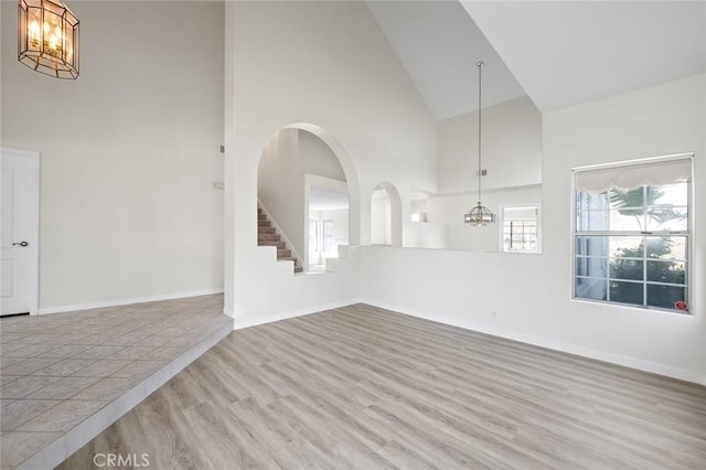 interior space featuring high vaulted ceiling, a notable chandelier, baseboards, and wood finished floors