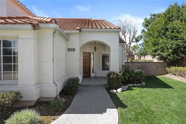 doorway to property with a yard, stucco siding, a tile roof, and fence