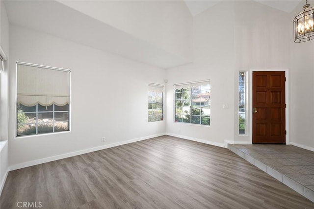 entrance foyer with a notable chandelier, high vaulted ceiling, wood finished floors, and baseboards