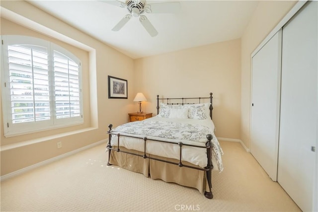 bedroom featuring a closet, light carpet, baseboards, and a ceiling fan