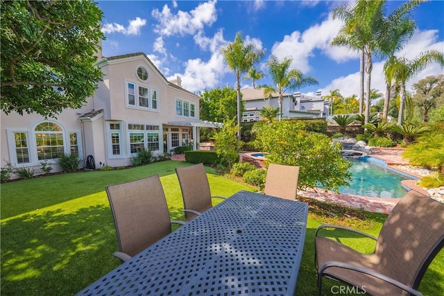 rear view of house featuring stucco siding, an outdoor pool, and a yard