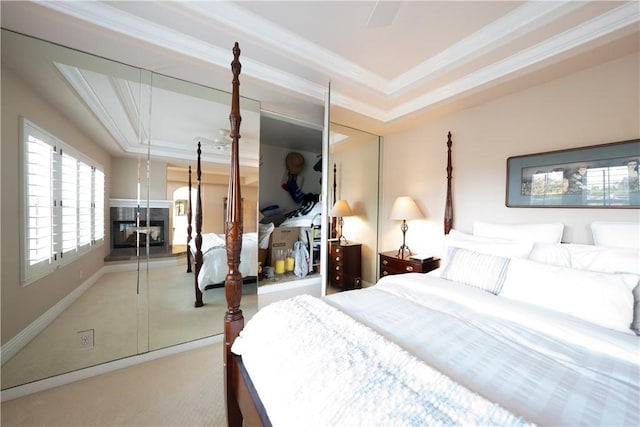 bedroom featuring a multi sided fireplace, a raised ceiling, carpet, and ornamental molding