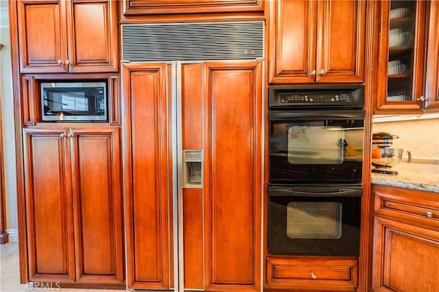 kitchen with light stone counters, paneled built in fridge, dobule oven black, stainless steel microwave, and backsplash