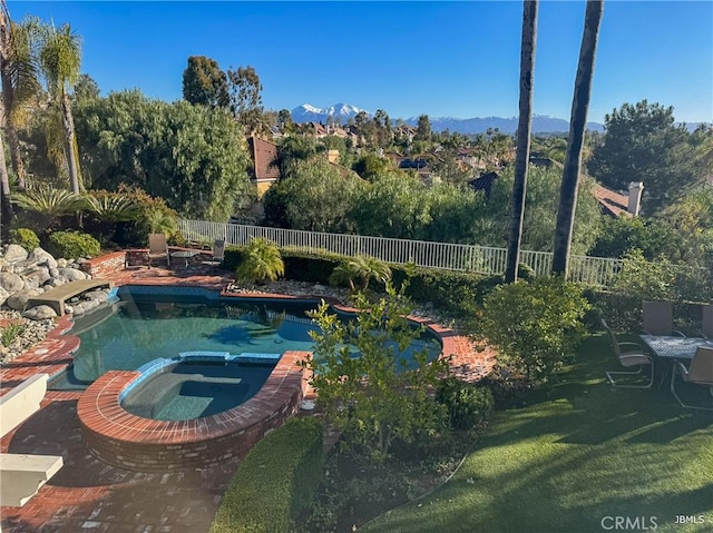 view of swimming pool with a mountain view, a pool with connected hot tub, and a fenced backyard