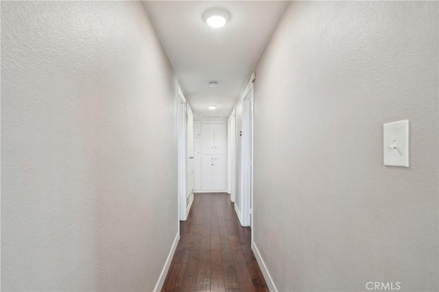 hallway featuring baseboards and dark wood-style flooring