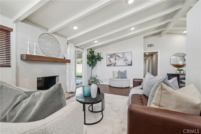 living area with vaulted ceiling with beams, recessed lighting, visible vents, a glass covered fireplace, and wood finished floors