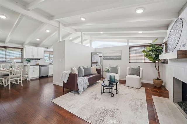 living room with lofted ceiling with beams, dark wood-style flooring, a tiled fireplace, and baseboards