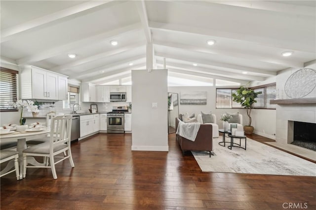 kitchen with dark wood-style floors, vaulted ceiling with beams, appliances with stainless steel finishes, open floor plan, and a sink