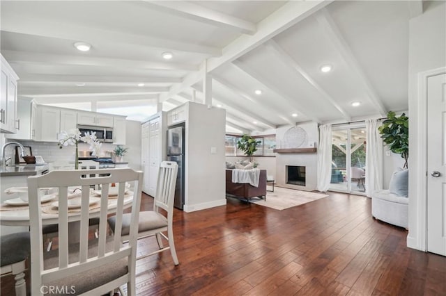 dining room featuring lofted ceiling with beams, a large fireplace, baseboards, and dark wood-type flooring