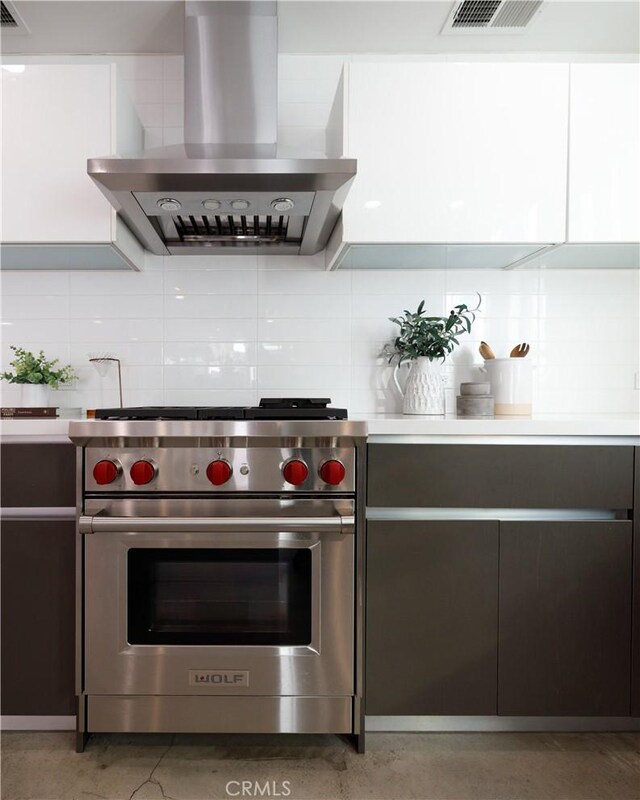 kitchen with wall chimney range hood, designer stove, visible vents, and decorative backsplash