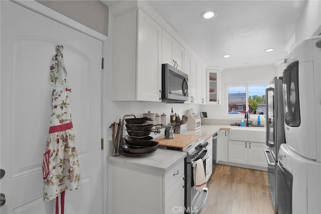 kitchen with stacked washer and dryer, light wood-style flooring, stainless steel appliances, light countertops, and white cabinetry