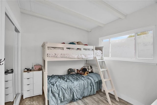 bedroom with beamed ceiling, wood finished floors, and baseboards