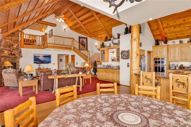 dining area featuring a fireplace, a ceiling fan, wood ceiling, high vaulted ceiling, and stairs