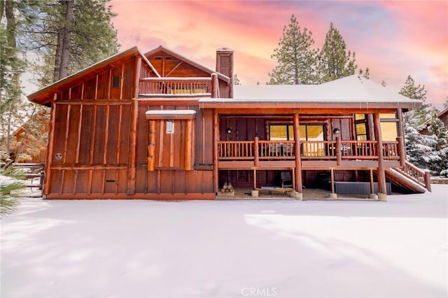 snow covered property with stairs and a chimney