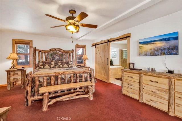 bedroom with ceiling fan, dark colored carpet, a barn door, and ensuite bath