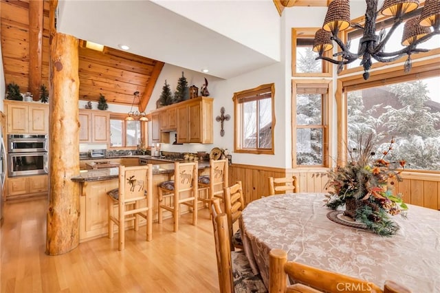 dining room featuring a wainscoted wall, wood walls, lofted ceiling, and light wood-style flooring