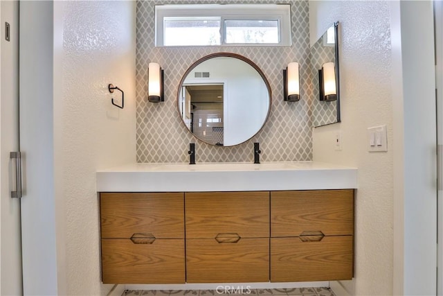 bathroom with visible vents, decorative backsplash, vanity, and a textured wall