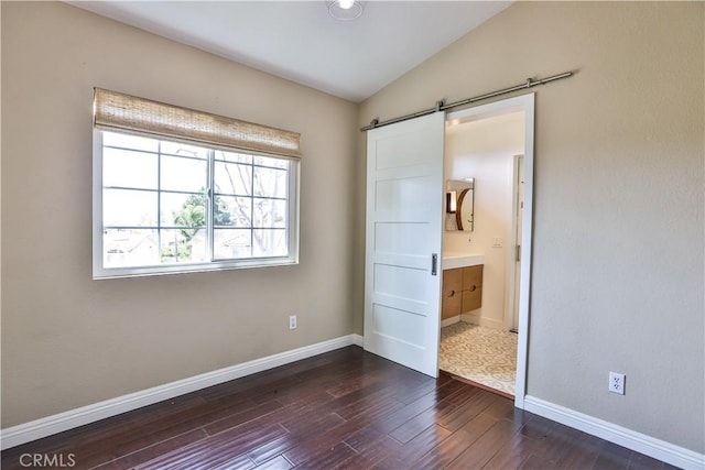 unfurnished bedroom featuring a barn door, baseboards, dark wood-style flooring, and lofted ceiling