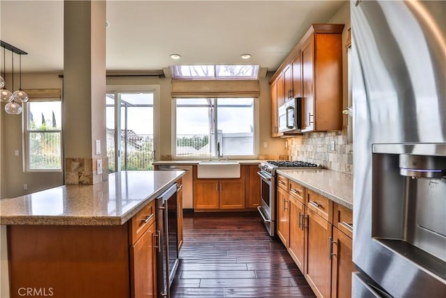 kitchen with backsplash, beverage cooler, brown cabinetry, stainless steel appliances, and a sink