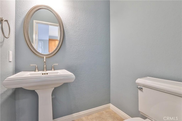 half bath with toilet, baseboards, and a textured wall