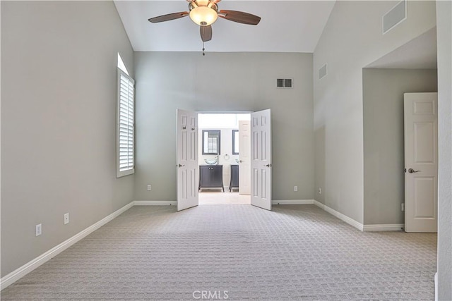 unfurnished bedroom featuring baseboards, visible vents, ceiling fan, a towering ceiling, and light carpet