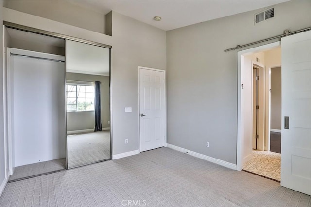 unfurnished bedroom with baseboards, visible vents, carpet floors, a closet, and a barn door