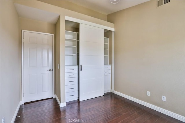 unfurnished bedroom featuring visible vents, baseboards, dark wood-type flooring, and a closet