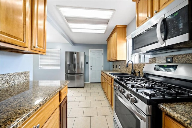 kitchen with light tile patterned floors, a sink, appliances with stainless steel finishes, dark stone counters, and tasteful backsplash