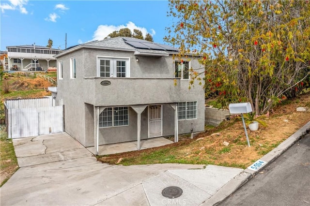 view of front of property featuring roof mounted solar panels, fence, and stucco siding