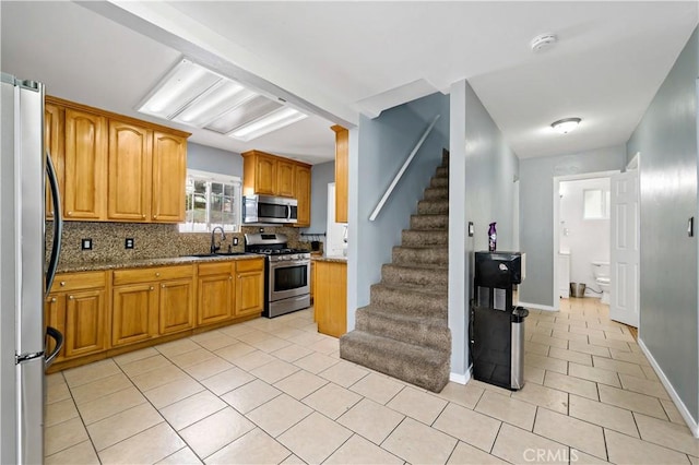 kitchen featuring stainless steel appliances, backsplash, light tile patterned flooring, a sink, and light stone countertops