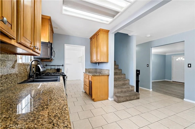 kitchen featuring light tile patterned floors, a sink, decorative backsplash, brown cabinetry, and dark stone countertops