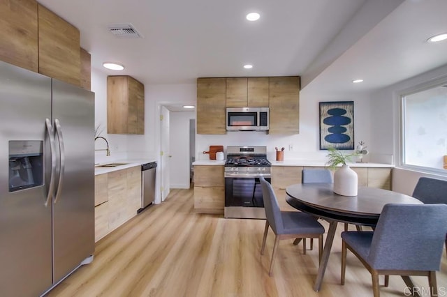 kitchen with stainless steel appliances, a sink, light wood-style floors, light countertops, and modern cabinets