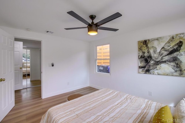 bedroom with a ceiling fan, visible vents, baseboards, and wood finished floors