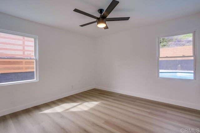 unfurnished room with light wood-type flooring, a ceiling fan, and baseboards