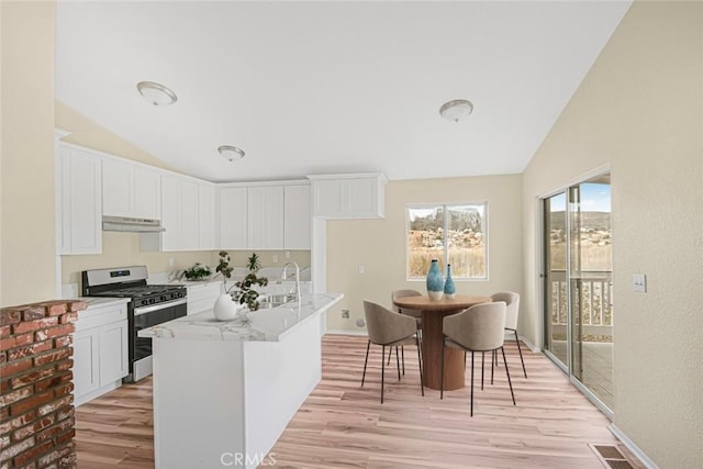 kitchen with under cabinet range hood, stainless steel range with gas cooktop, lofted ceiling, and a sink