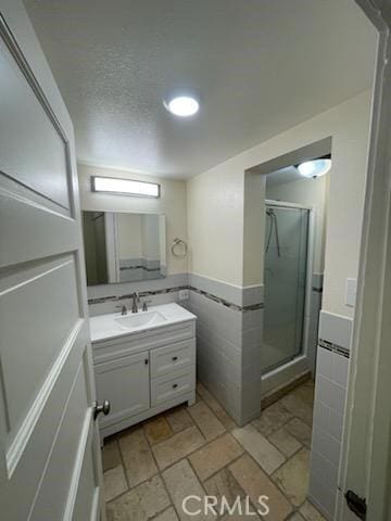 bathroom featuring vanity, tile walls, a stall shower, and a textured ceiling