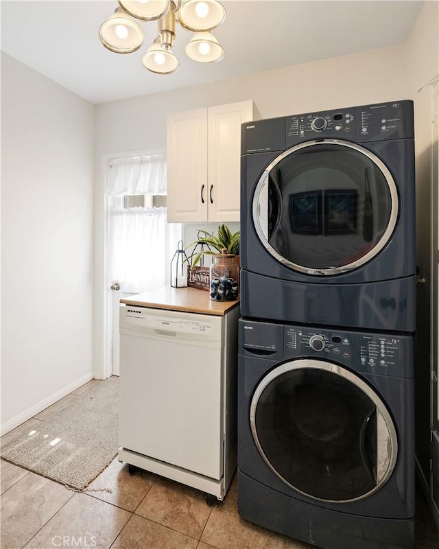 laundry room featuring a notable chandelier, light tile patterned floors, stacked washer / drying machine, laundry area, and baseboards